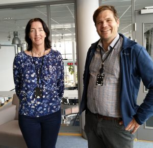 Kvinne og mann innendørs ser rett i kamera og smiler. 