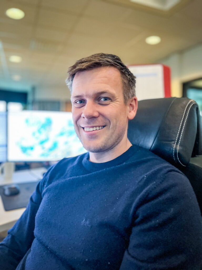 Portrett av mann  i blå genser med operasjonsroms-bakgrunn