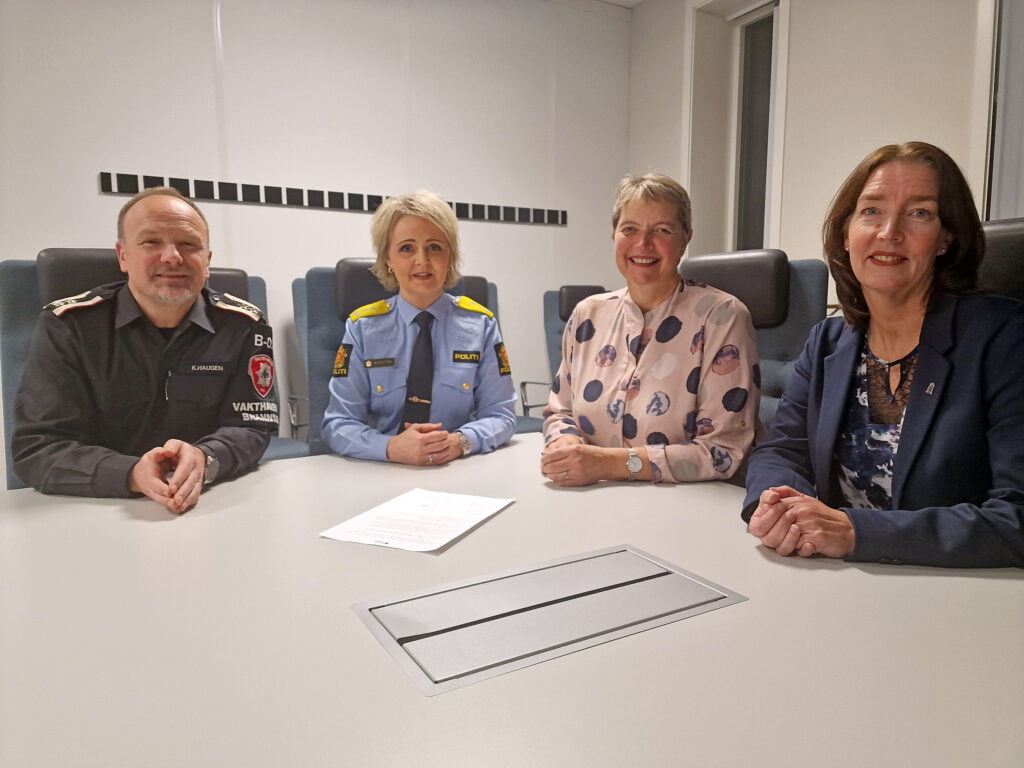 Tre kvinner og en mann sitter ved et bord og ser på fotograf etter å ha signert en avtale.