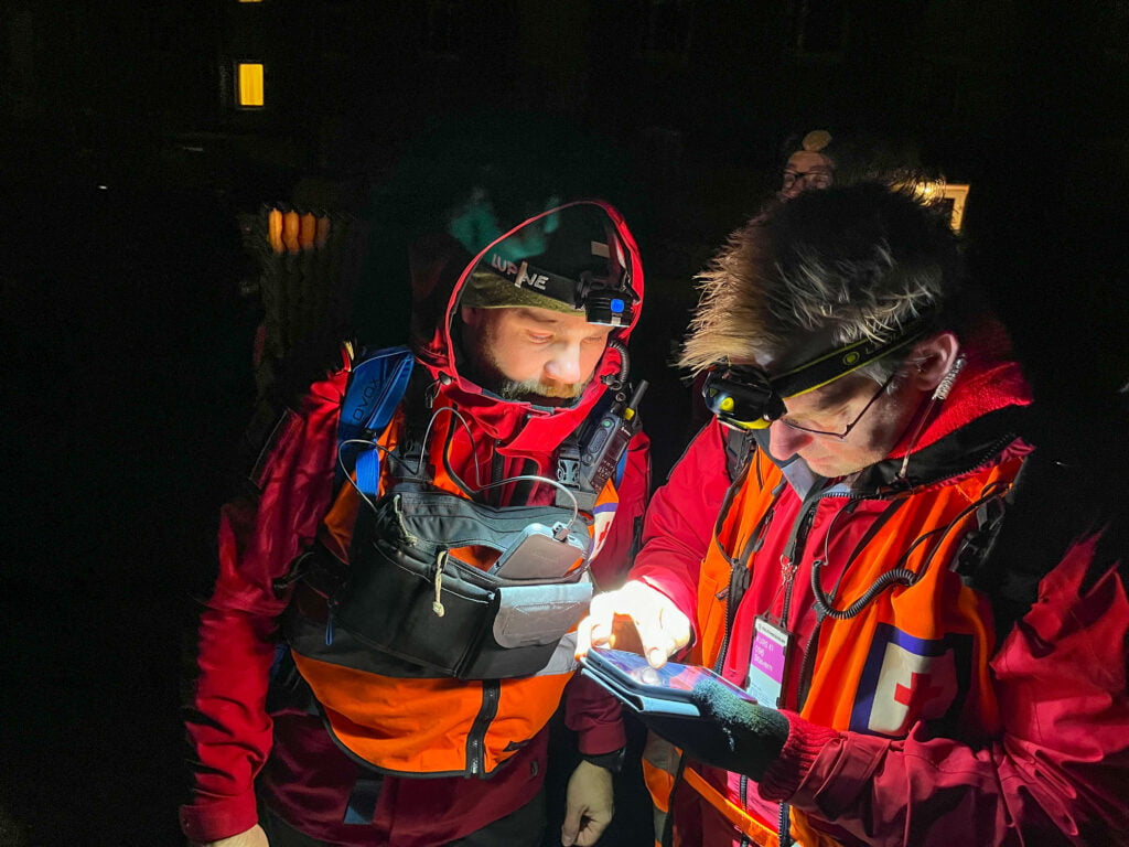 To mennesker er ute på leteaksjon i mørket. De har på hodelykter og ser på en mobiltelefon.