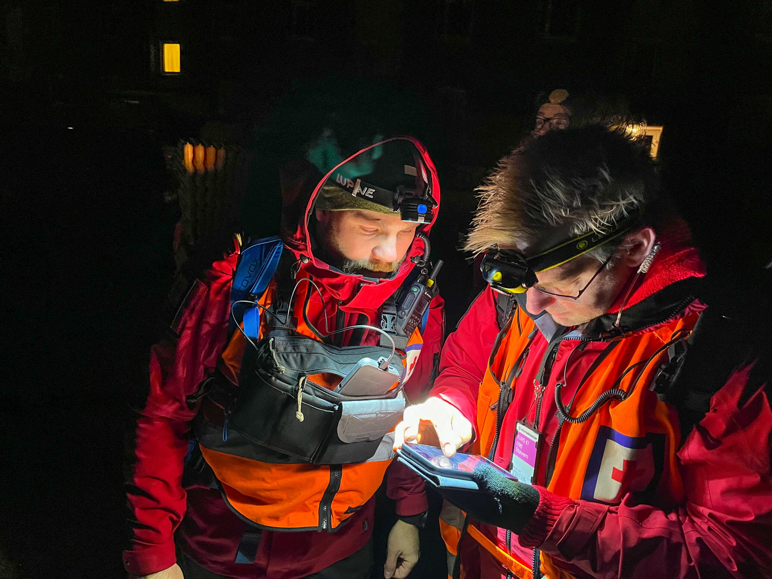 To mennesker er ute på leteaksjon i mørket. De har på hodelykter og ser på en mobiltelefon.