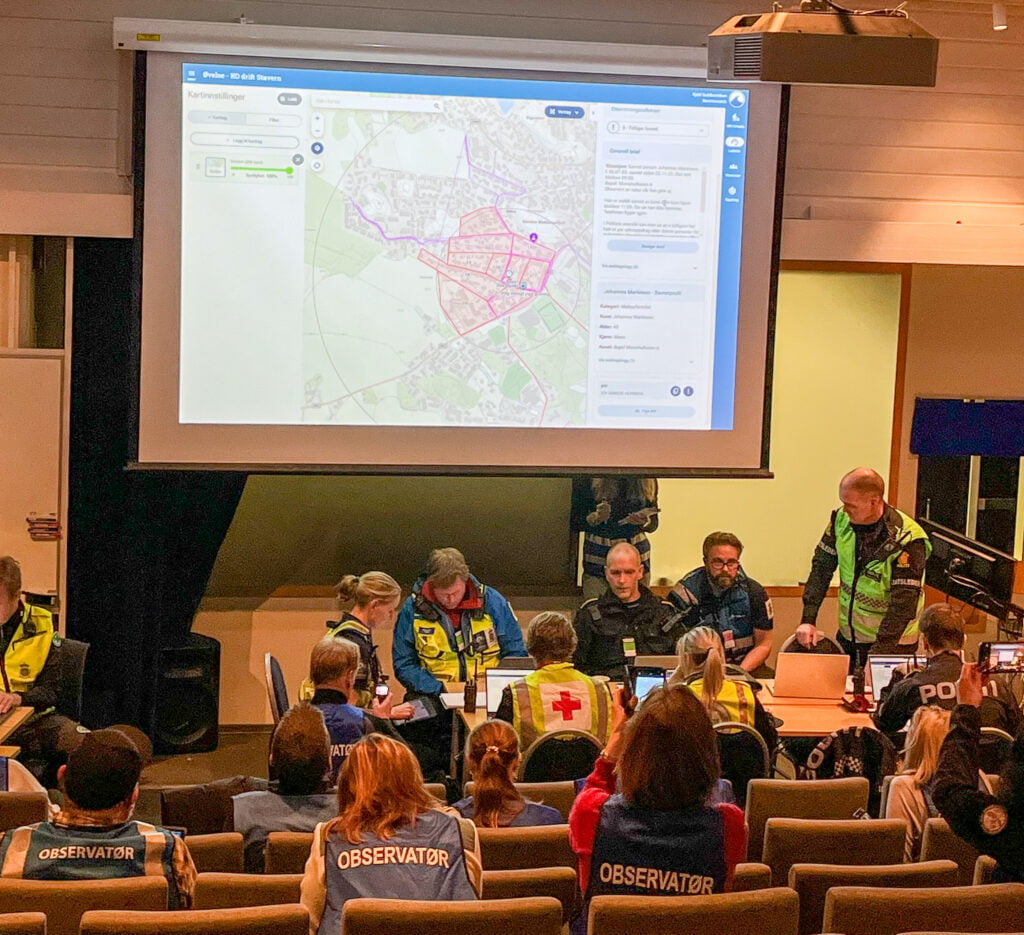 En gruppe frivillige, politi og observatører ser på et kart på en storskjerm i et auditorium