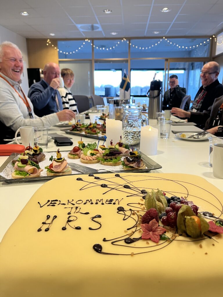 Et bord med en kake på og smilende mennesker i bakgrunnen