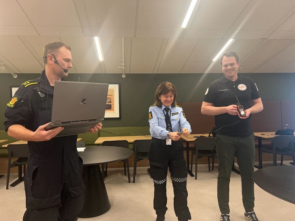 Tre mennesker på rekke. En holder en pc, e holder en bærbar liten gps og kvinnen i midten klipper en ledning som går mellom PC og GPS.