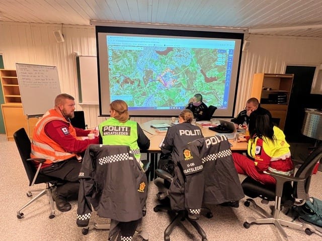 En gruppe med frivillige redningsmannskaper og politi sitter rundt et bord.