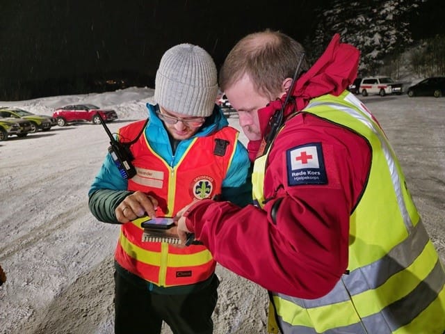 To frivillige redningsmannskaper ser sammen på en mobiltelefon utendørs.