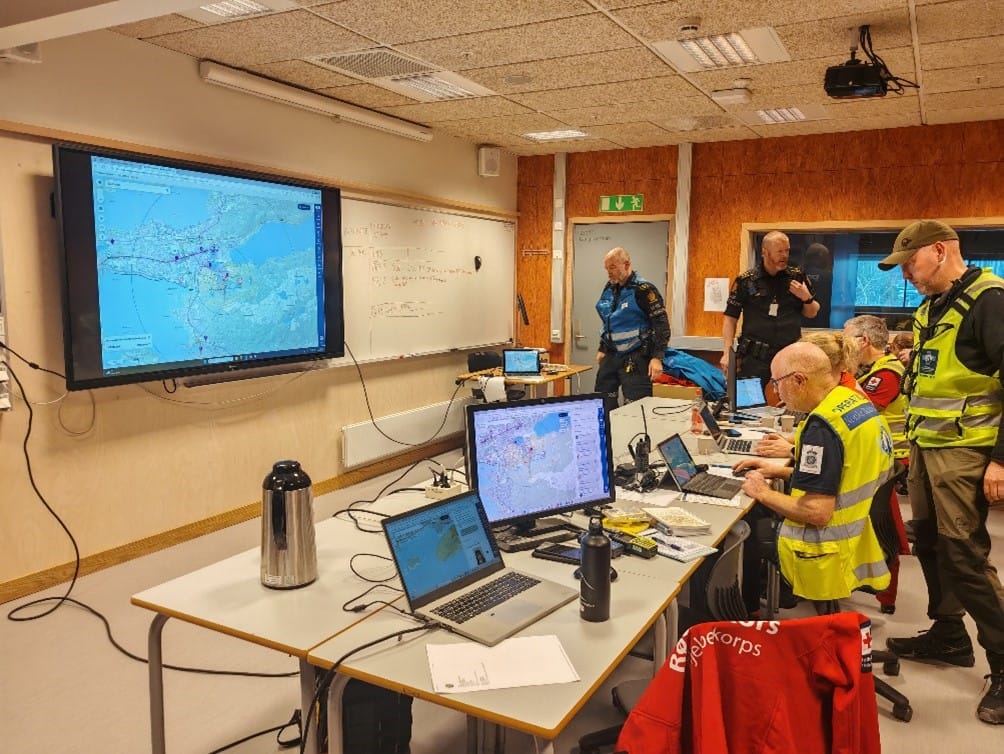 En gruppe mennesker, frivillige og politi, jobber sammen inn i en kommandosentral. 