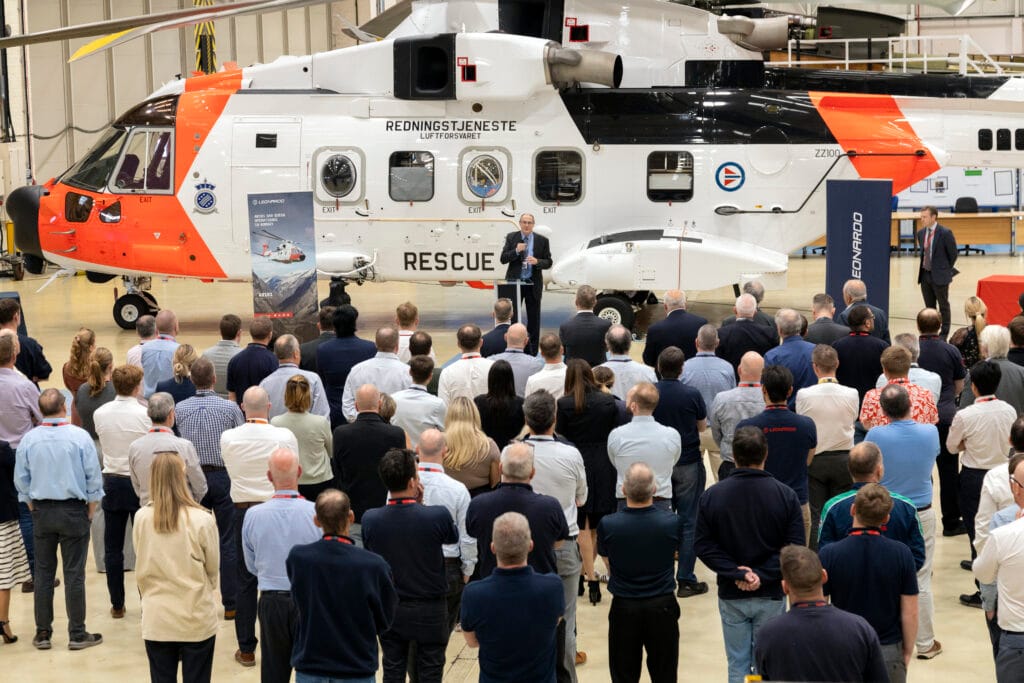 Mennesker i forkant av et helikopter ser på en mann som holder en tale