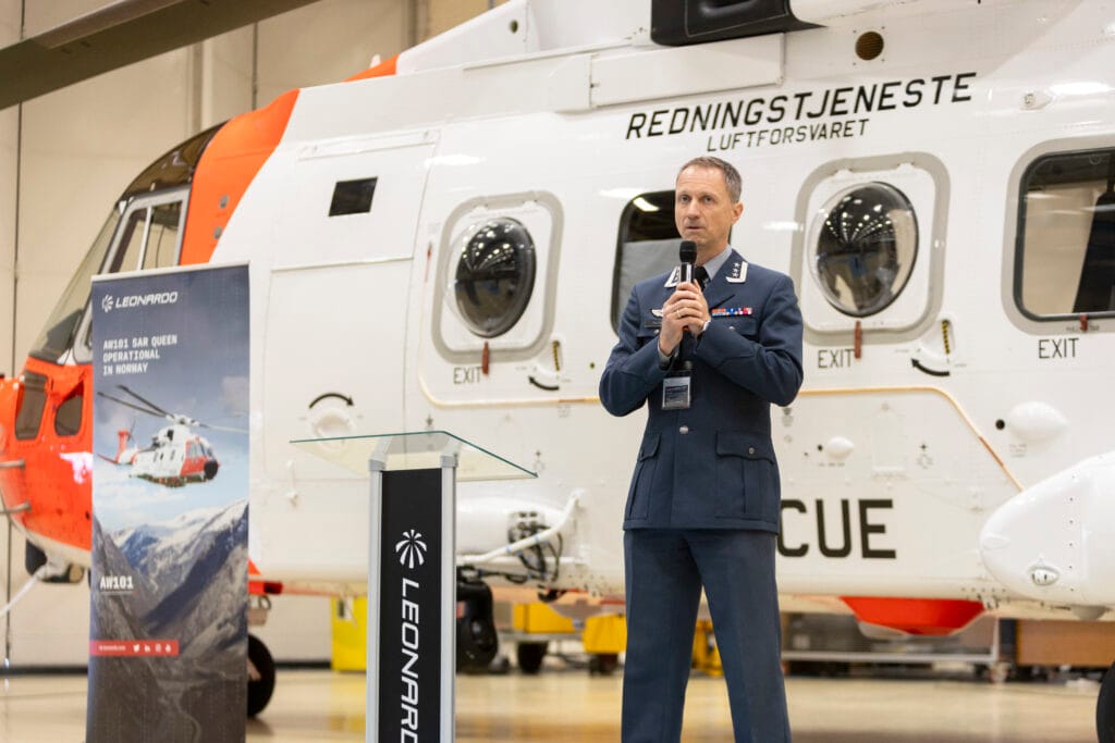 Mann i militær uniform foran redningshelikopter inni en hall
