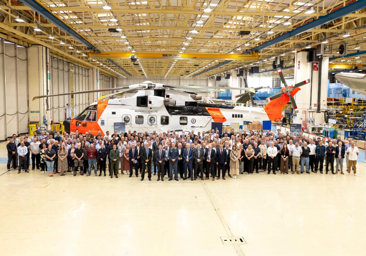 En veldig stor gruppe mennesker står foran et helikpoter inni en produksjonshall.