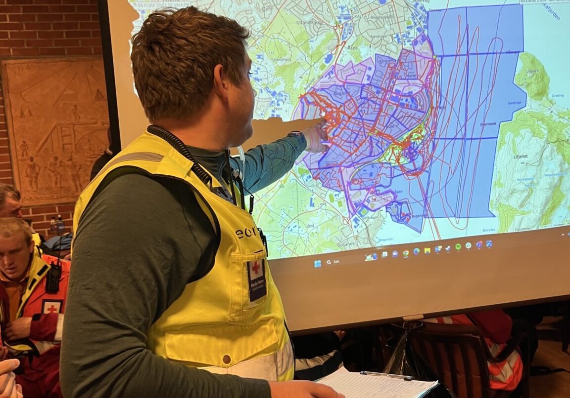 En mann som er frivillig redningsmannskap peker på en skjerm med et kart.