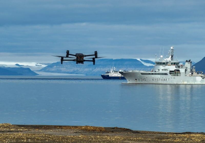 Kystvaktskip, drone og ekspedisjonsskip ligger i en fjord på Svalbard