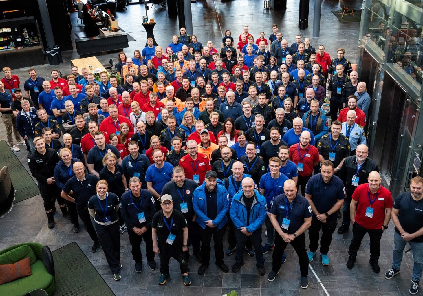 Stor gruppe mennesker står samlet tett i tett og ser på fotograf som står en etasje opp
