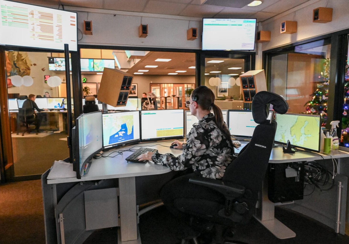 Kvinne sitter ved pult med mange dataskjermer.