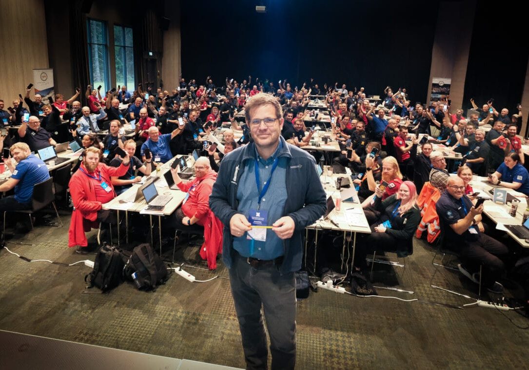 Mann holder blyant foran forsamling av mennesker i en sal som holder opp mobiltelefoner.