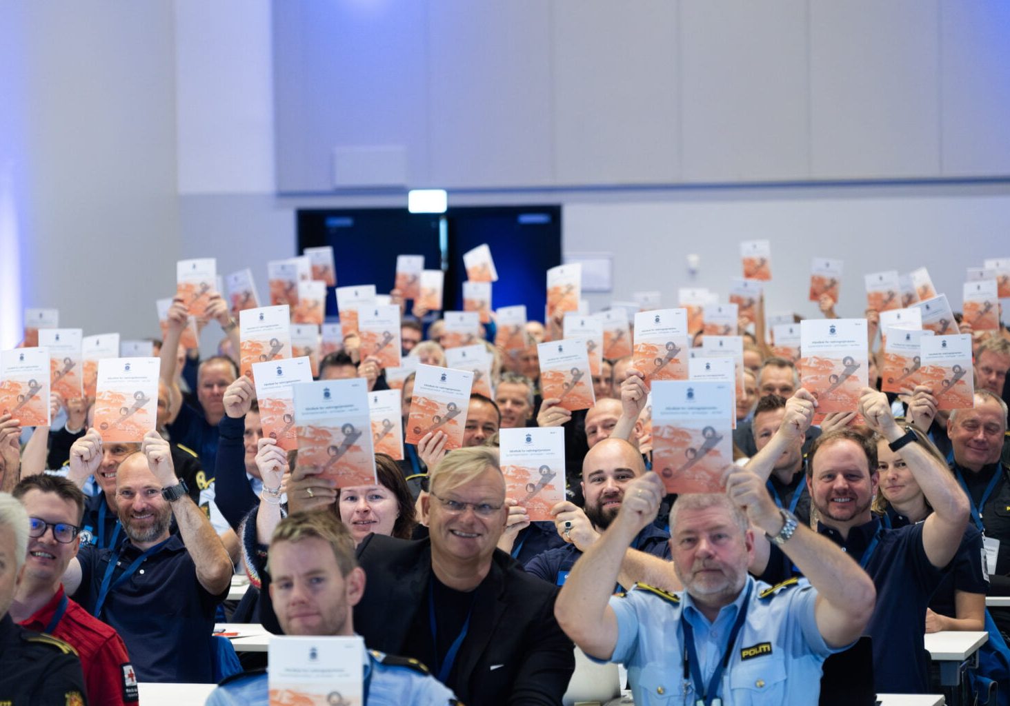 Mennesker i sal holder opp en publikasjon mens de smiler.