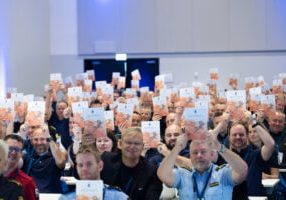 Mennesker i sal holder opp en publikasjon mens de smiler.