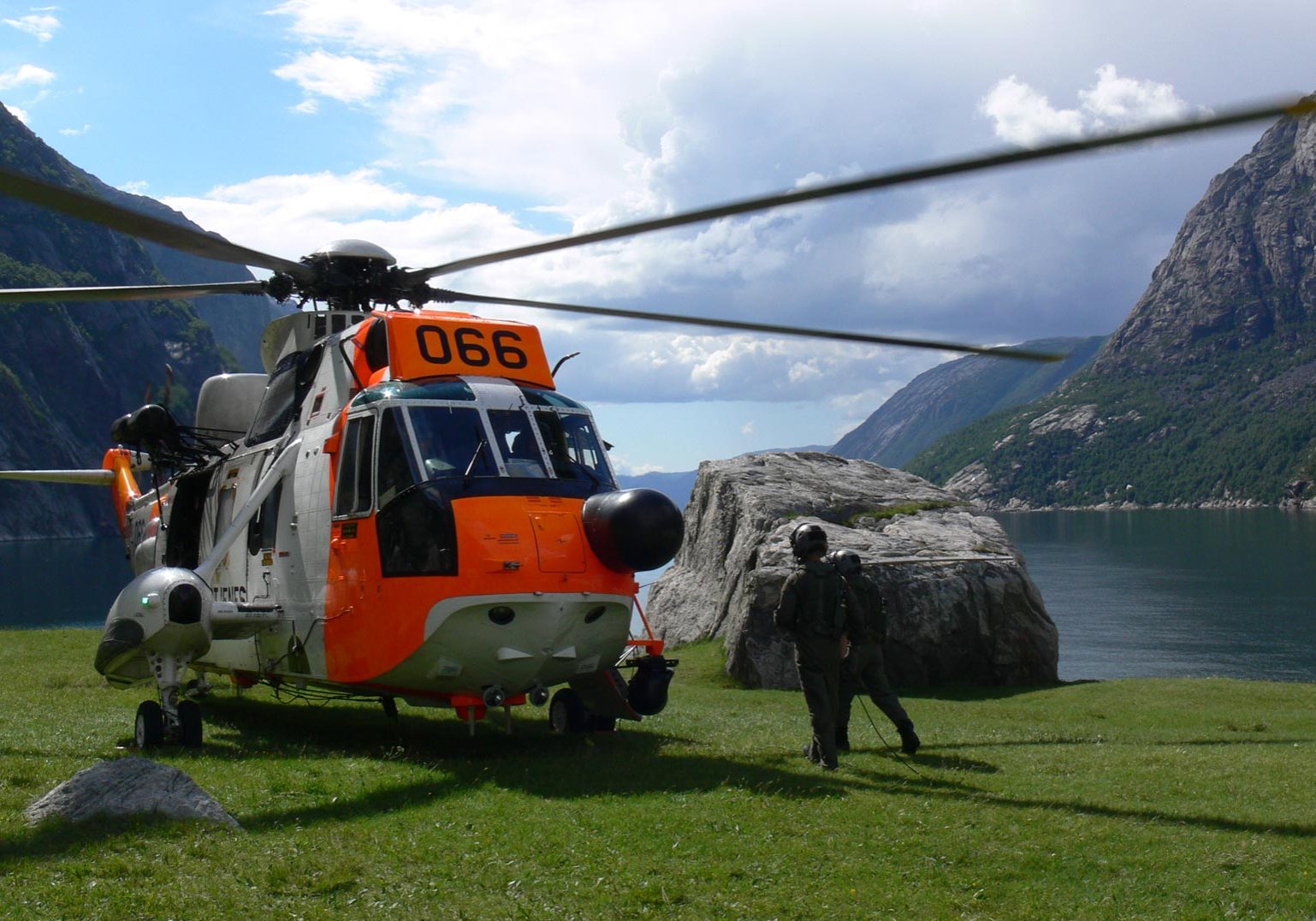 Seaking helikopter og to personer med fjell og fjord i bakgrunn.