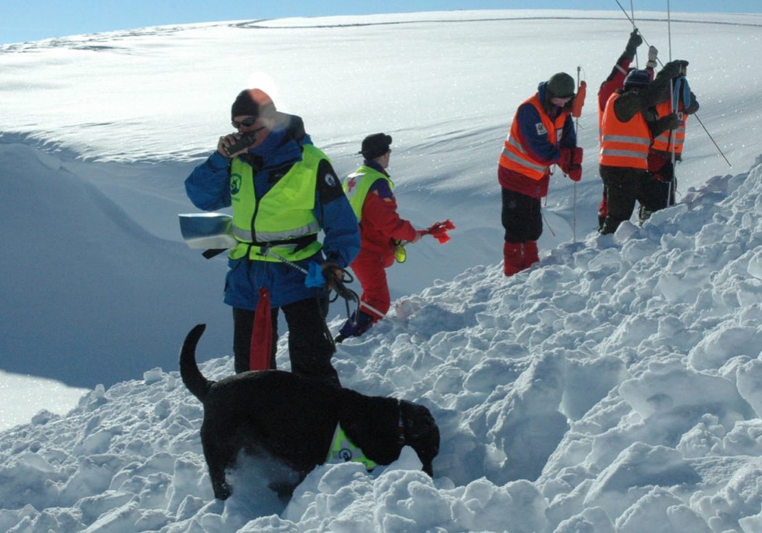 redningsaksjon i snøskred, mann snakker i walkie-talkie og flere graver bak han.