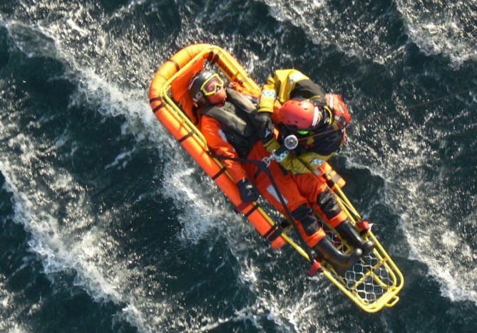 Mann ligger i redningsbåre på vei opp i et helikopter